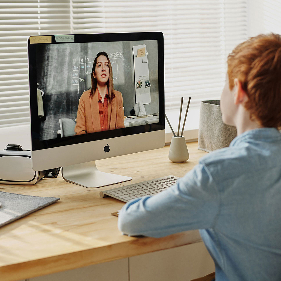 ein Junge sitzt am Schreibtisch und nimmt an einem Video Call auf einem iMac teil